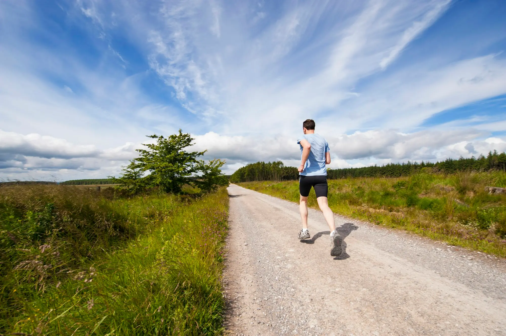 Coureur en t-shirt bleu sur un chemin de campagne sous un grand ciel nuageux