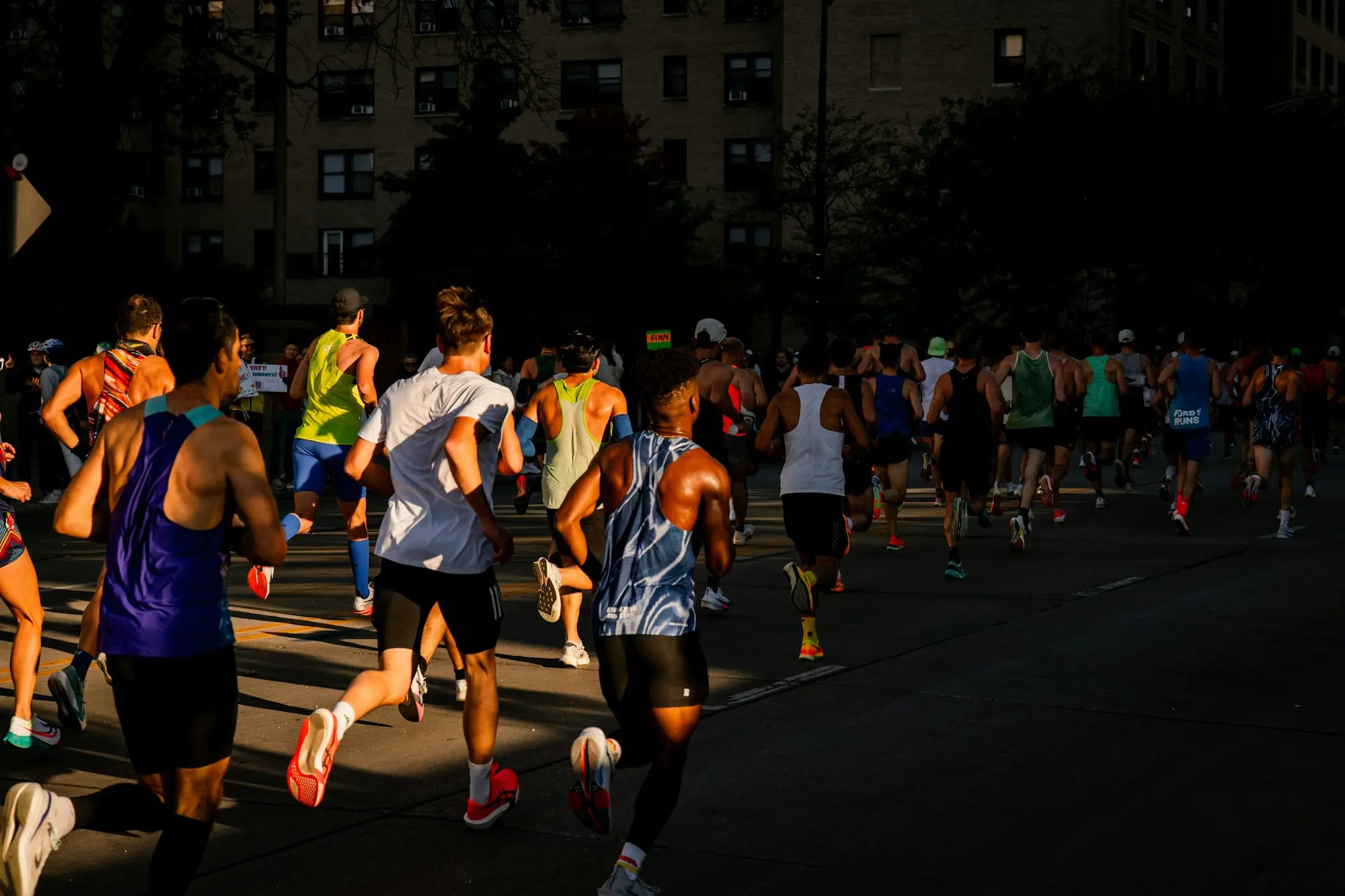 Peloton de coureurs de marathon dans une avenue urbaine, éclairés par le soleil matinal