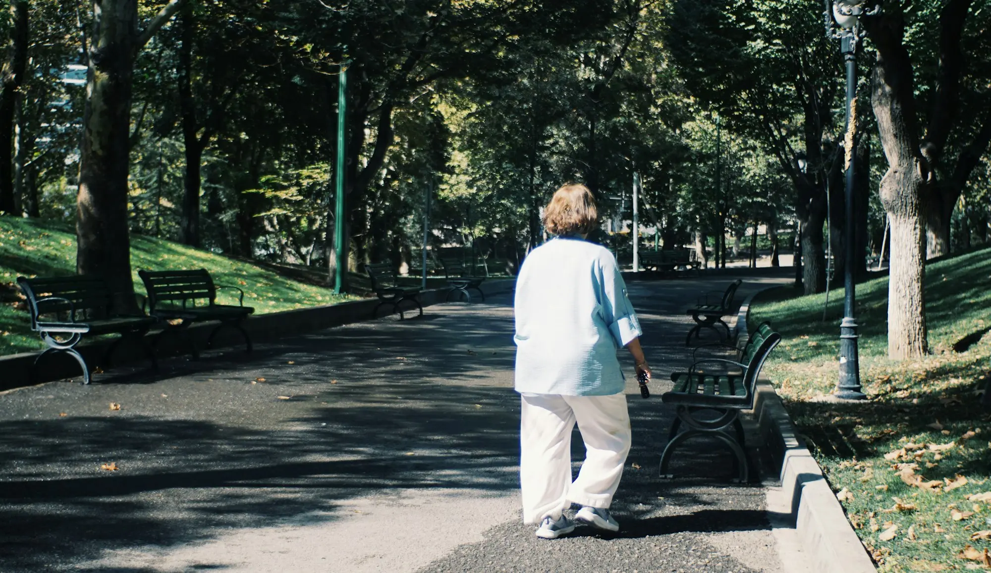 Femme qui marche d'un bon pas dans une allée ombragée d'un parc arboré