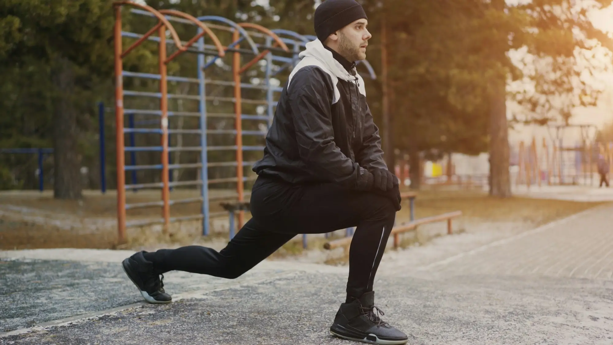 Sportif en tenue d'hiver qui fait des fentes pour s'échauffer dans un parc