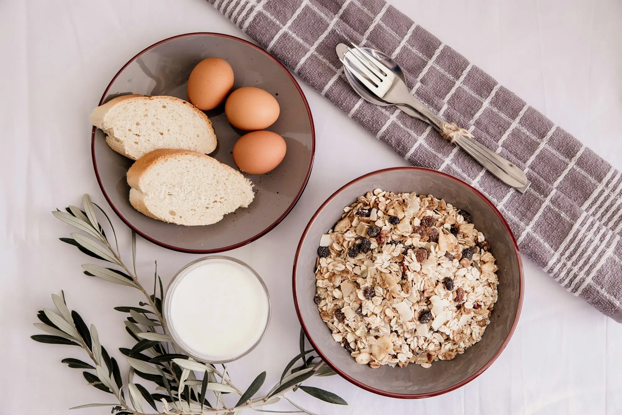 Petit-déjeuner complet avec œufs, pain, muesli et verre de lait sur une nappe claire